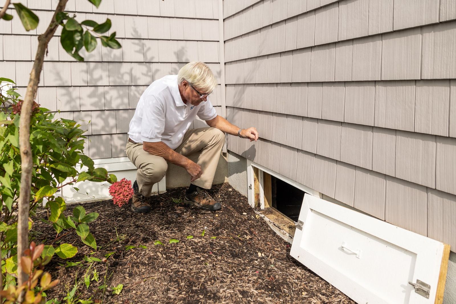 Inspector checking a crawl space opening outside a home