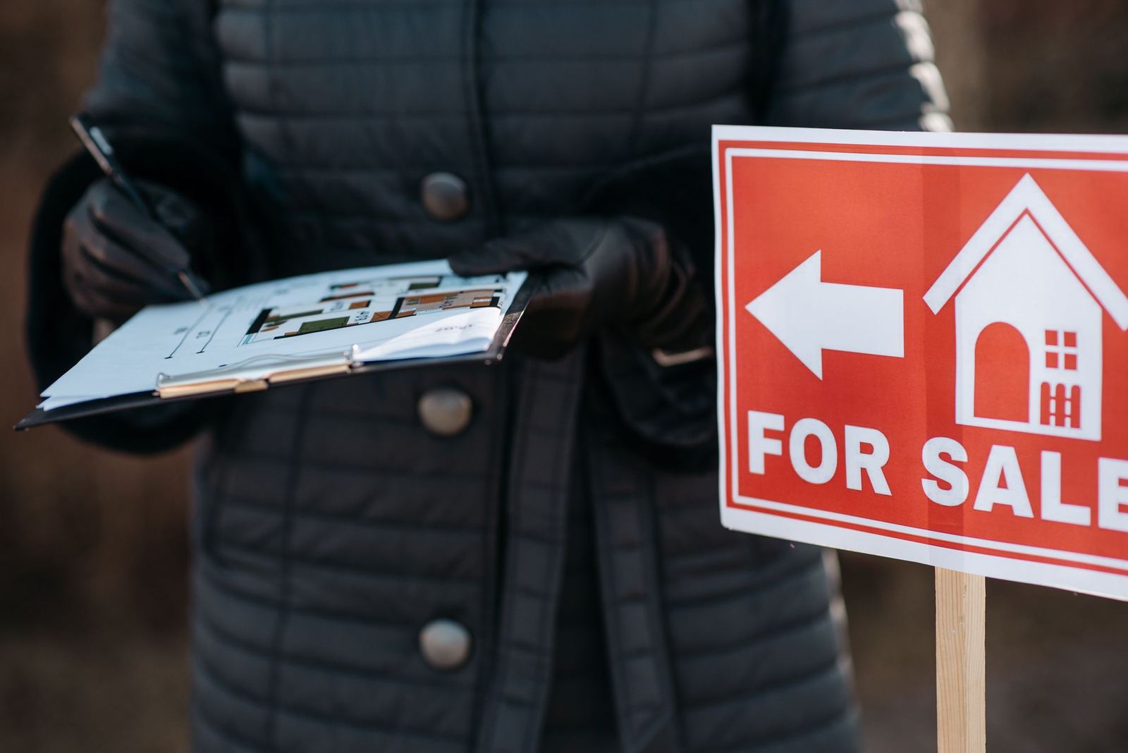 Agent holding paperwork beside a For Sale sign